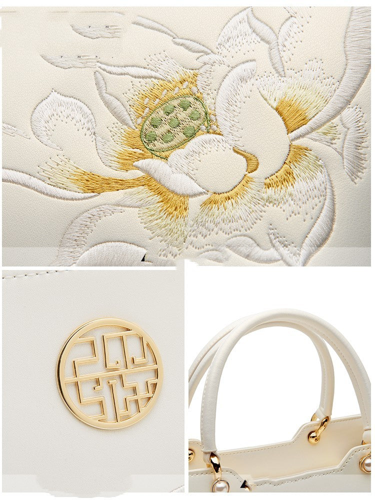 White handbag with gold accents and floral embroidery on a light gray background