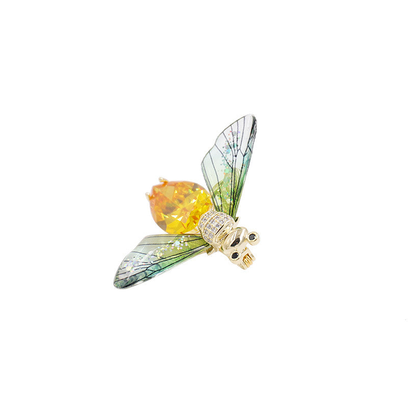 Decorative insect brooch with a yellow center and green wings on a white background