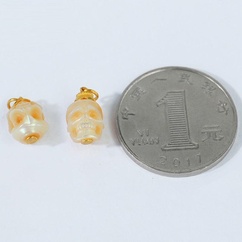 Two small skull-shaped pendants next to a Chinese yuan coin on a white background