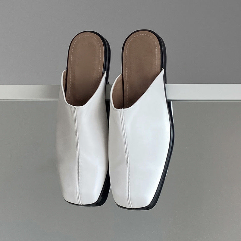 Pair of white leather mules with brown soles on a gray background