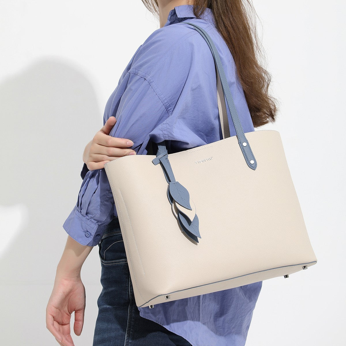 Person holding a beige tote bag with a brand logo on a white background