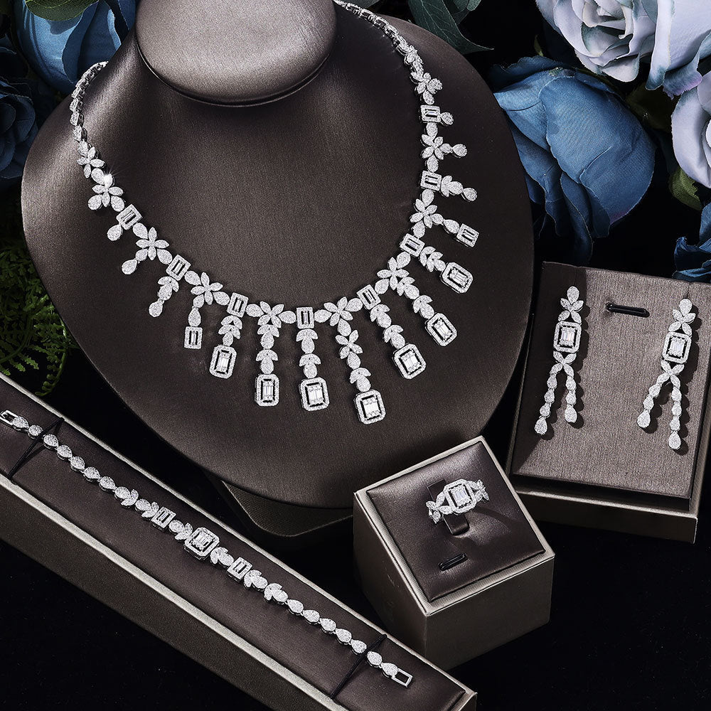 Jewelry set including a necklace, earrings, and ring on a dark surface with flowers in the background.