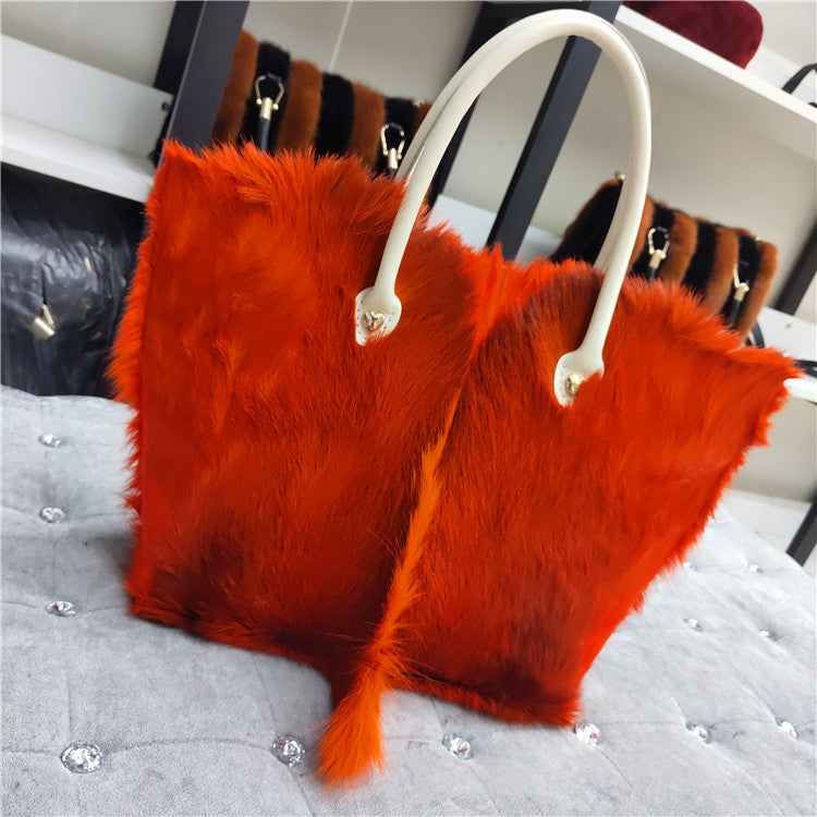Red fur handbag with white handle on a gray surface