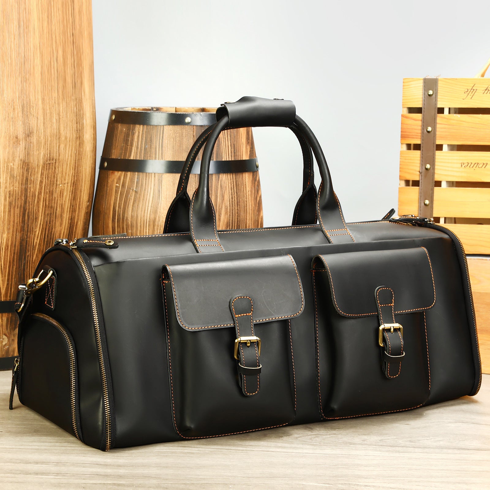 Black leather duffel bag with gold buckles on a wooden surface.