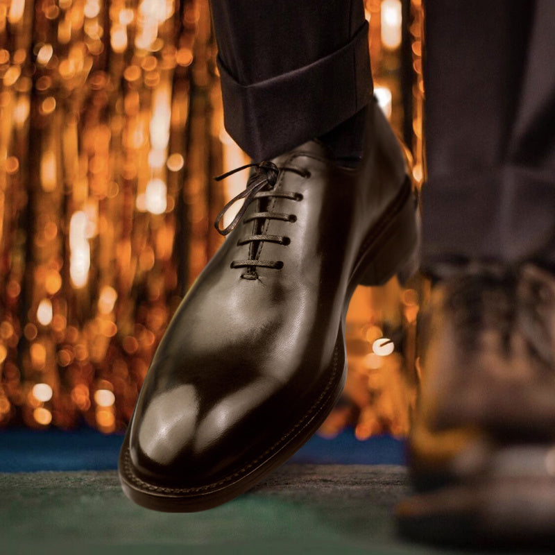 Close-up of a person wearing black dress shoes with a blurred, warm-toned background.