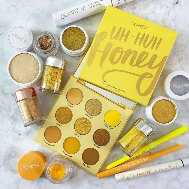 Makeup set with 'Uh-Huh Honey' palette and various cosmetic products on a marble surface