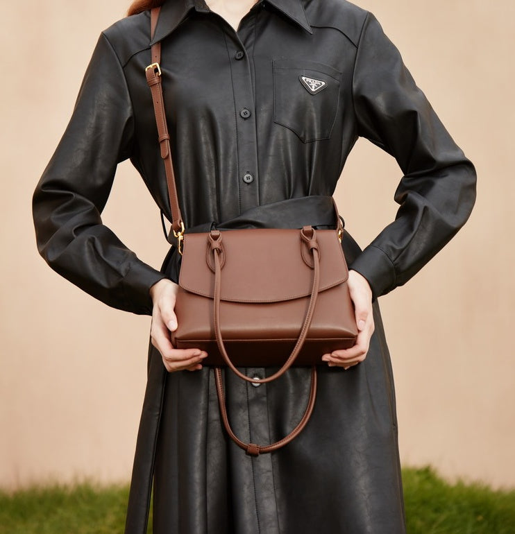 Person holding a brown leather handbag wearing a black coat with a brand logo.