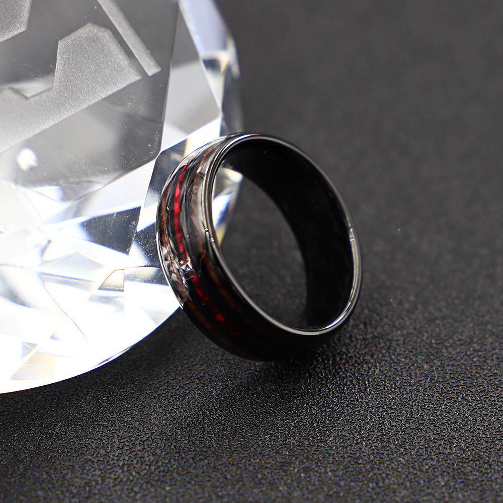 Black ring with red accents next to a large diamond on a dark surface