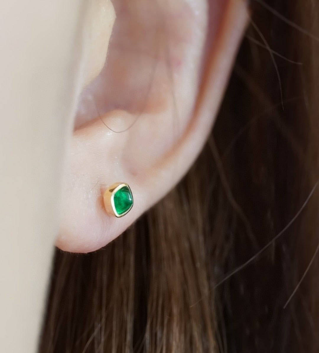 Close-up of an ear wearing a gold earring with a green gemstone.