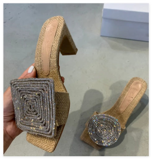 Brown sandal with decorative square buckle held by a hand on a gray floor.
