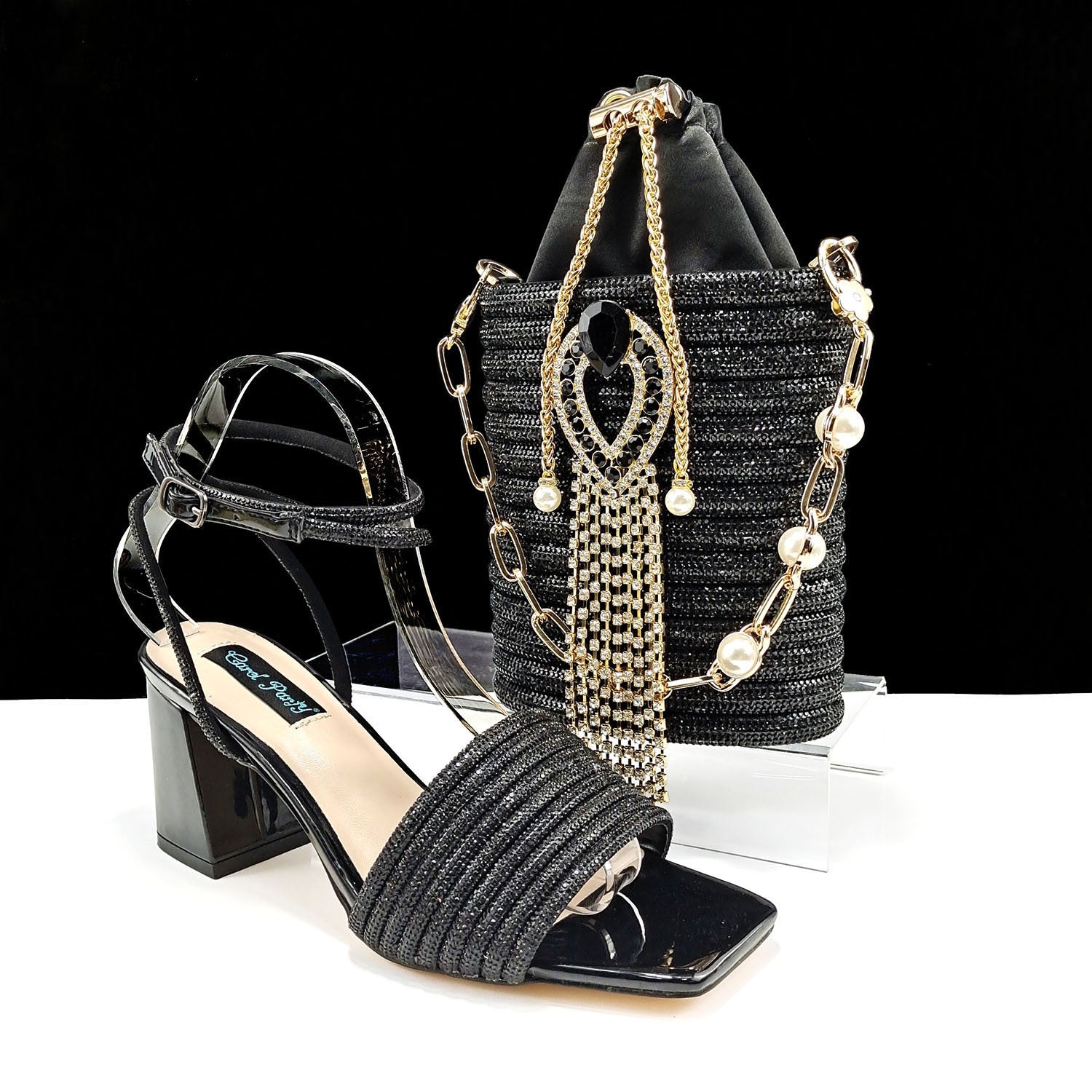 Black strappy sandal with high block heel and matching handbag on a white surface.