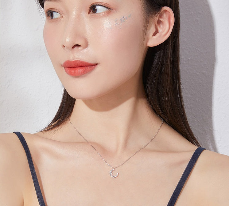 Close-up of a woman wearing a delicate necklace with a moon pendant against a neutral background