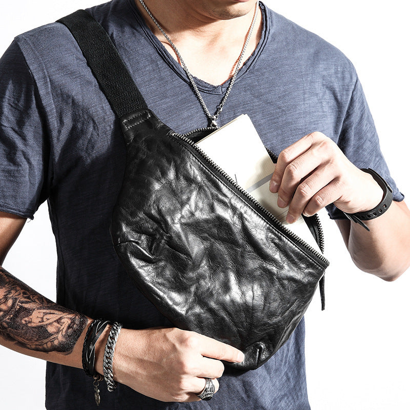Person wearing a black leather crossbody bag with a plain background