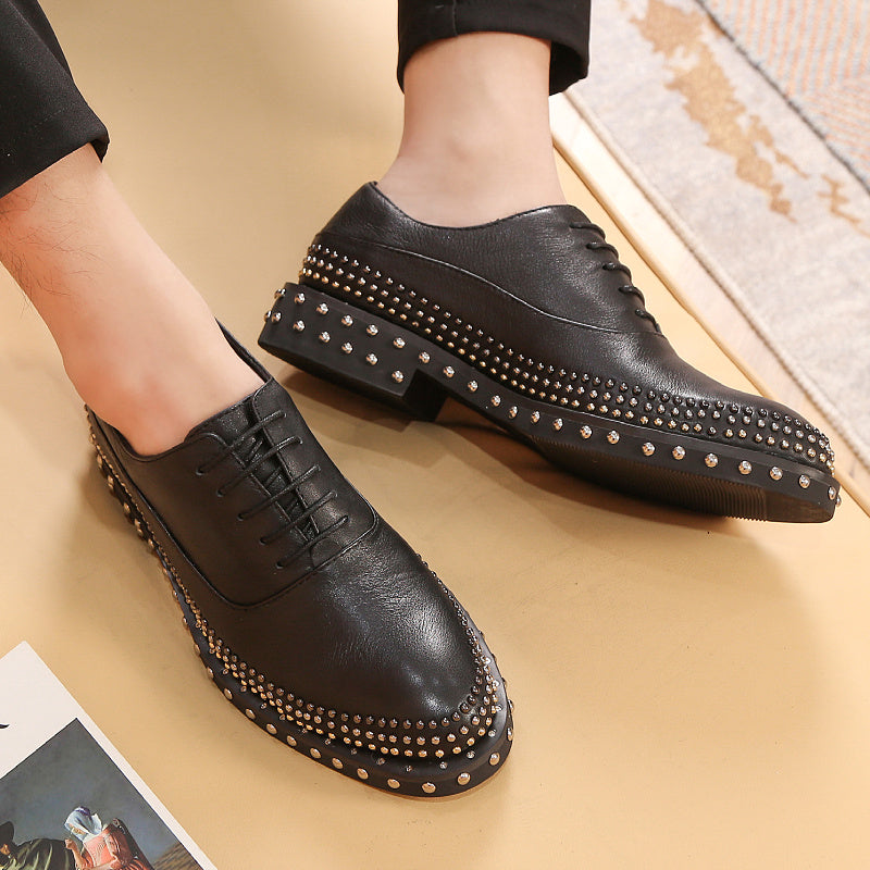 Black leather shoes with studded details on a beige surface
