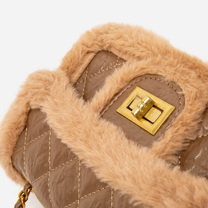 Close-up of a brown handbag with fur trim and gold clasp on a white background