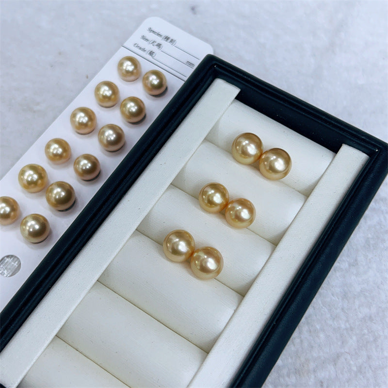 Gold pearl earrings in a display case on a light gray background