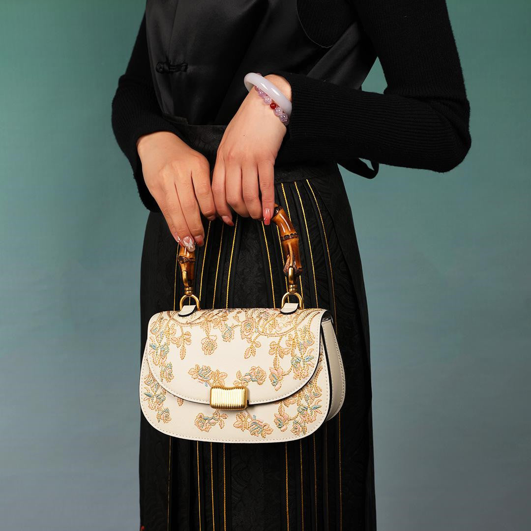 Person holding a white handbag with floral embroidery against a teal background