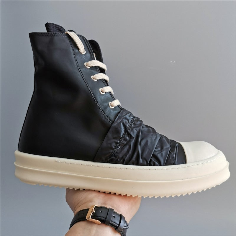 Black high-top sneaker with white sole held by a hand against a gray background
