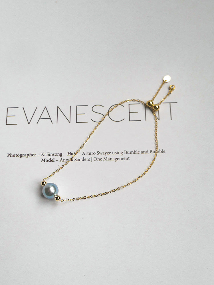 Gold bracelet with a pearl on a light gray background, featuring the brand 'Evanescent'.
