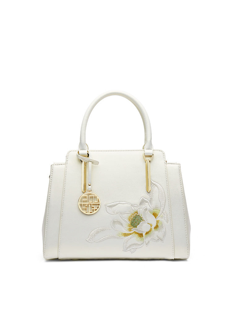 White handbag with floral design and gold accents on a white background