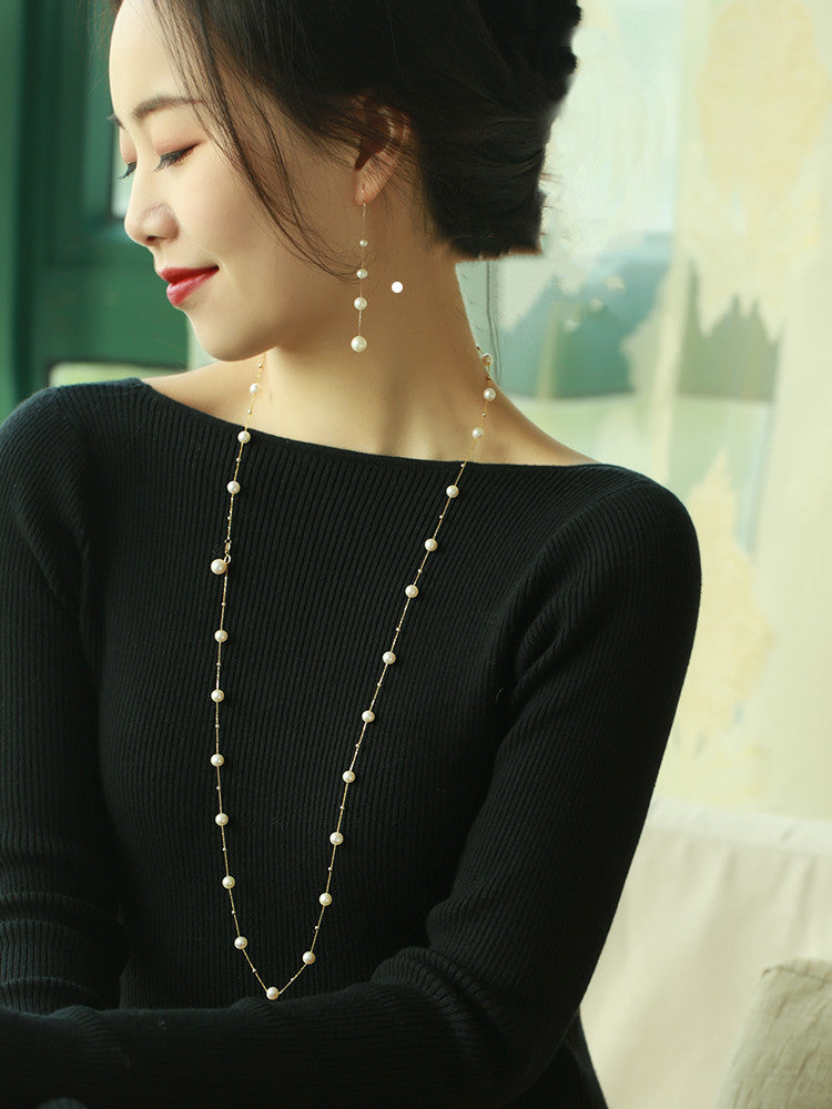 Woman wearing a long pearl necklace and earrings indoors
