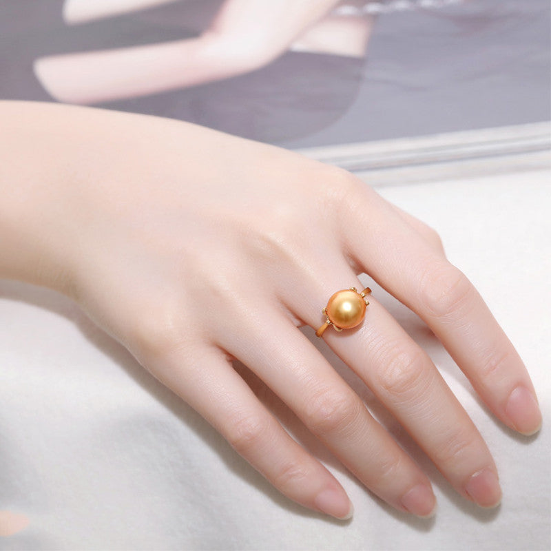 Gold ring with a pearl on a hand against a neutral background