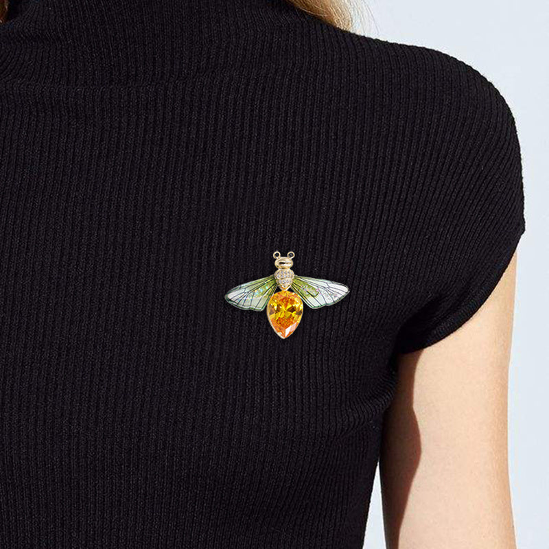 Person wearing a black sweater with a decorative insect brooch featuring a yellow center and green wings.