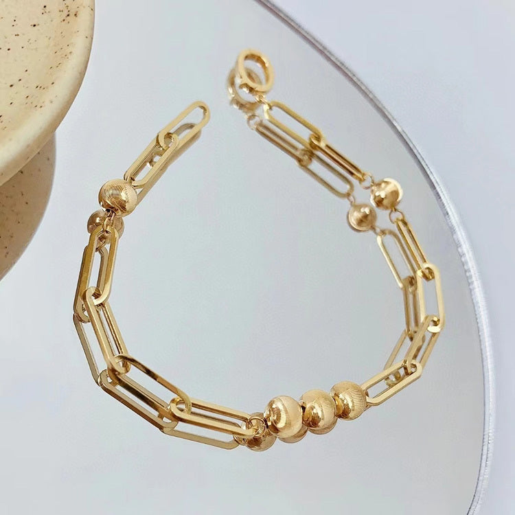 Gold bracelet with chain and bead design on a light background