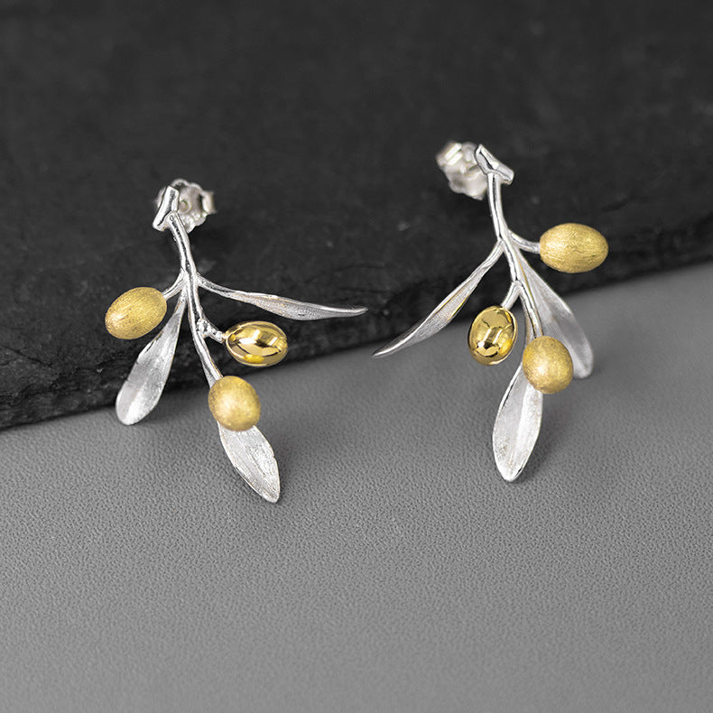 Silver and gold leaf earrings on a dark stone surface