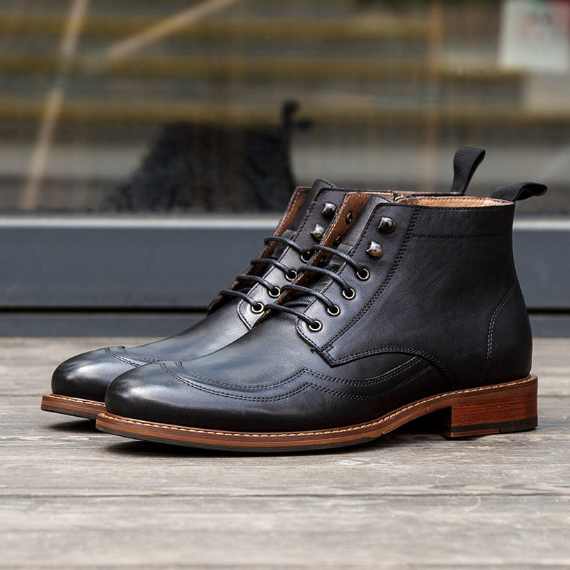 Pair of black leather boots with brown soles on a wooden surface.