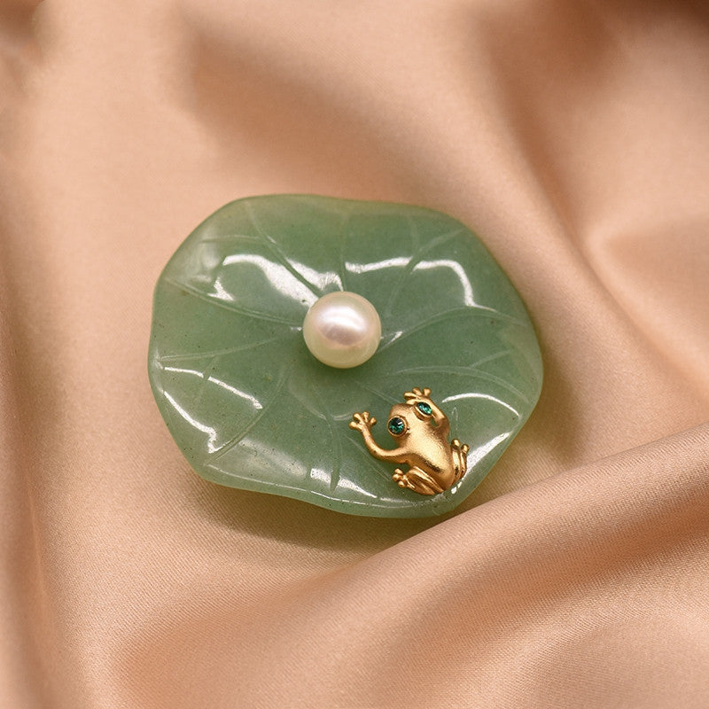 Jade brooch with a pearl and gold frog on a beige fabric background