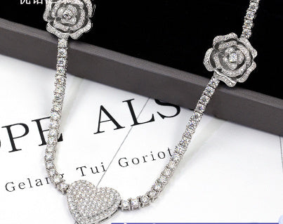 Silver necklace with floral and heart designs on a white background