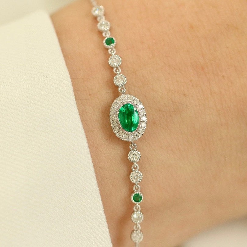 Delicate bracelet with emerald and diamond-like stones on a wrist against a neutral background