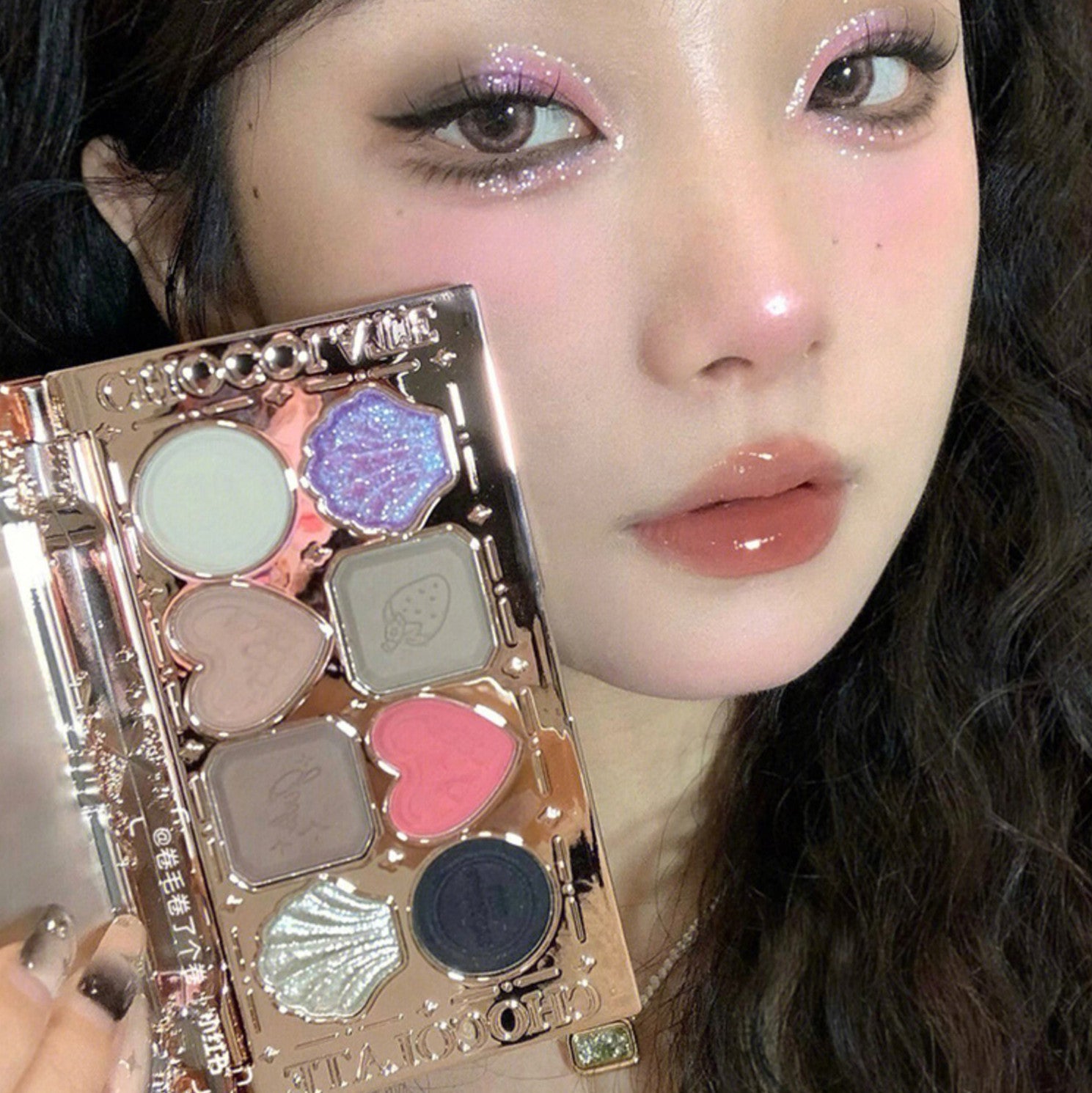 Makeup palette held by a person with glittery eye makeup