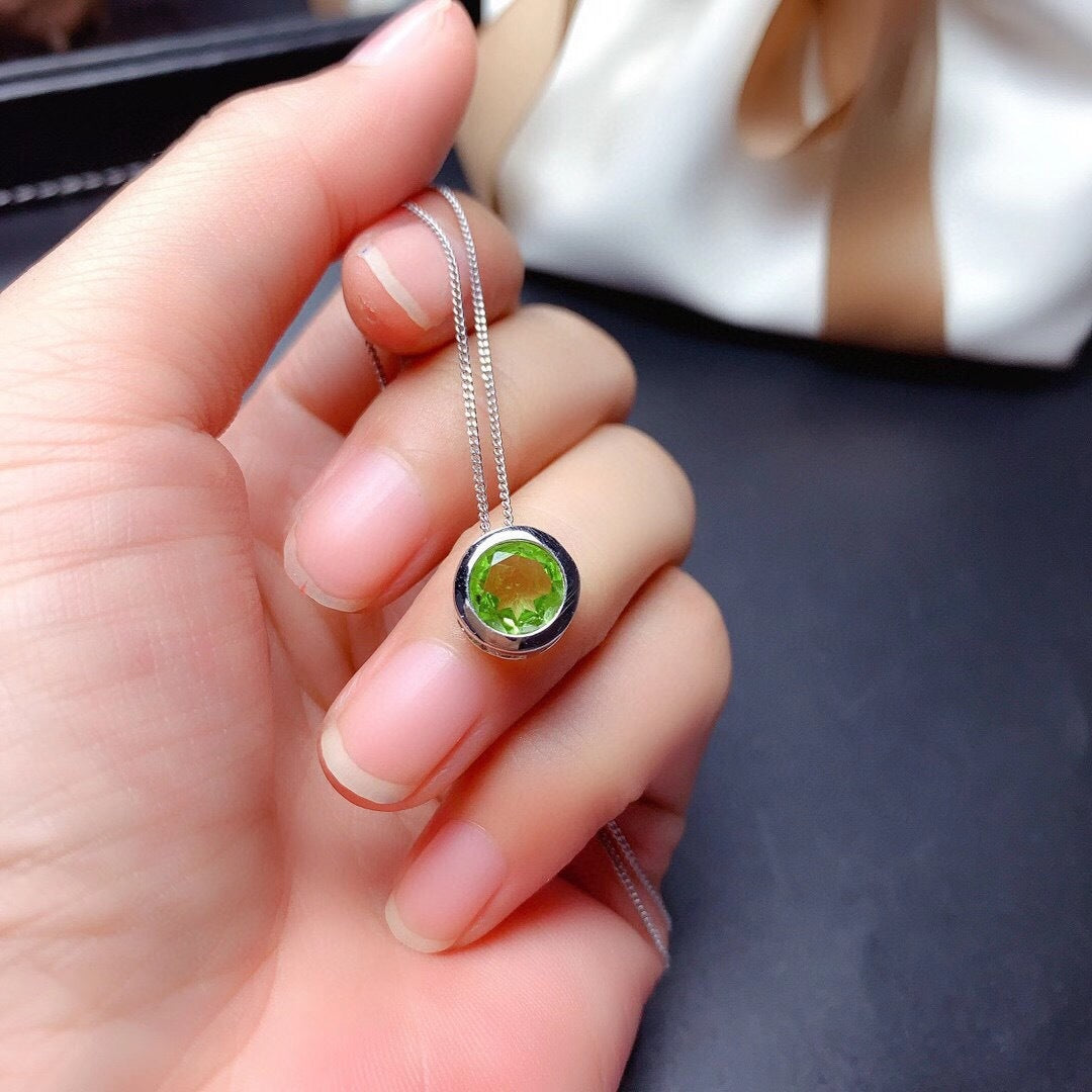 Hand holding a silver necklace with a green gemstone pendant.