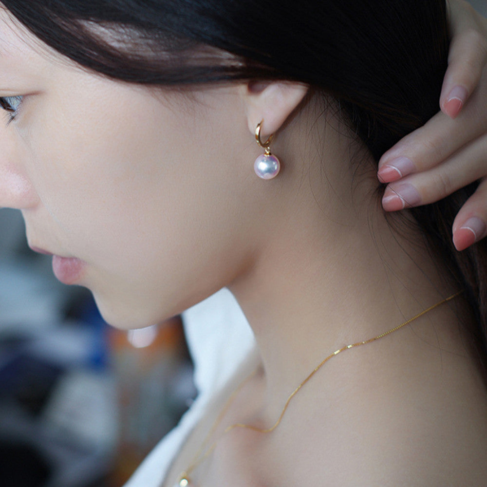 Close-up of a person wearing a gold earring with a pearl pendant.
