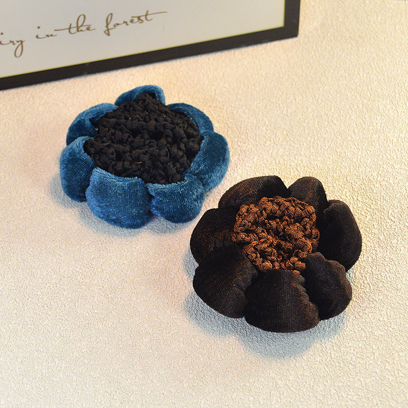 Two flower-shaped hair ties, one blue and one brown, on a textured surface.