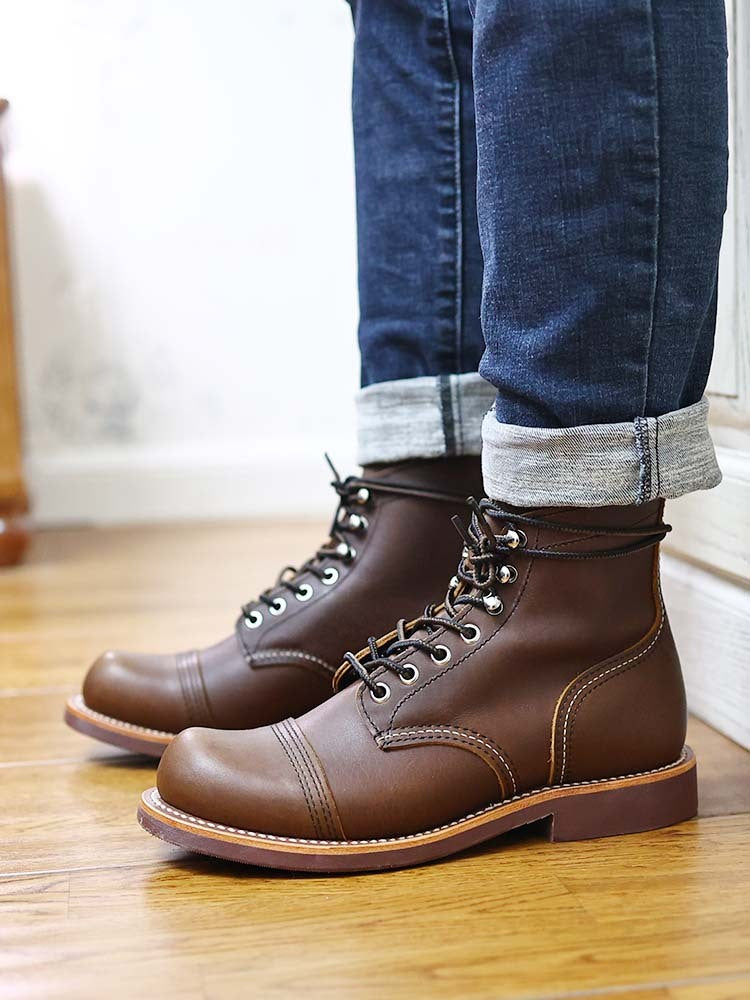 Brown leather boots worn with rolled-up jeans on a wooden floor.