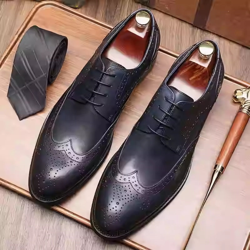 Pair of black dress shoes with a tie and shoe horn on a wooden surface
