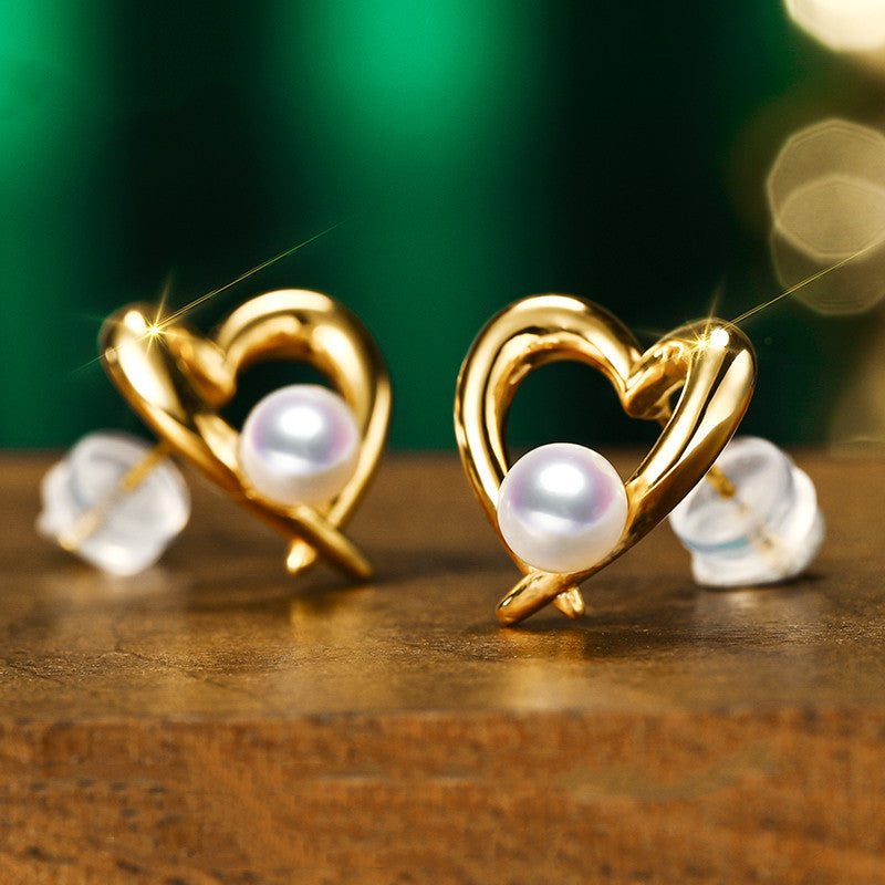 Gold heart-shaped earrings with pearls on a wooden surface