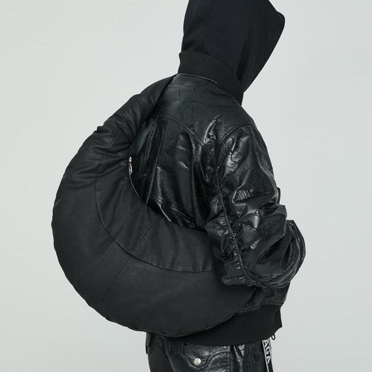 Person wearing a black quilted jacket holding a matching black bag against a light gray background