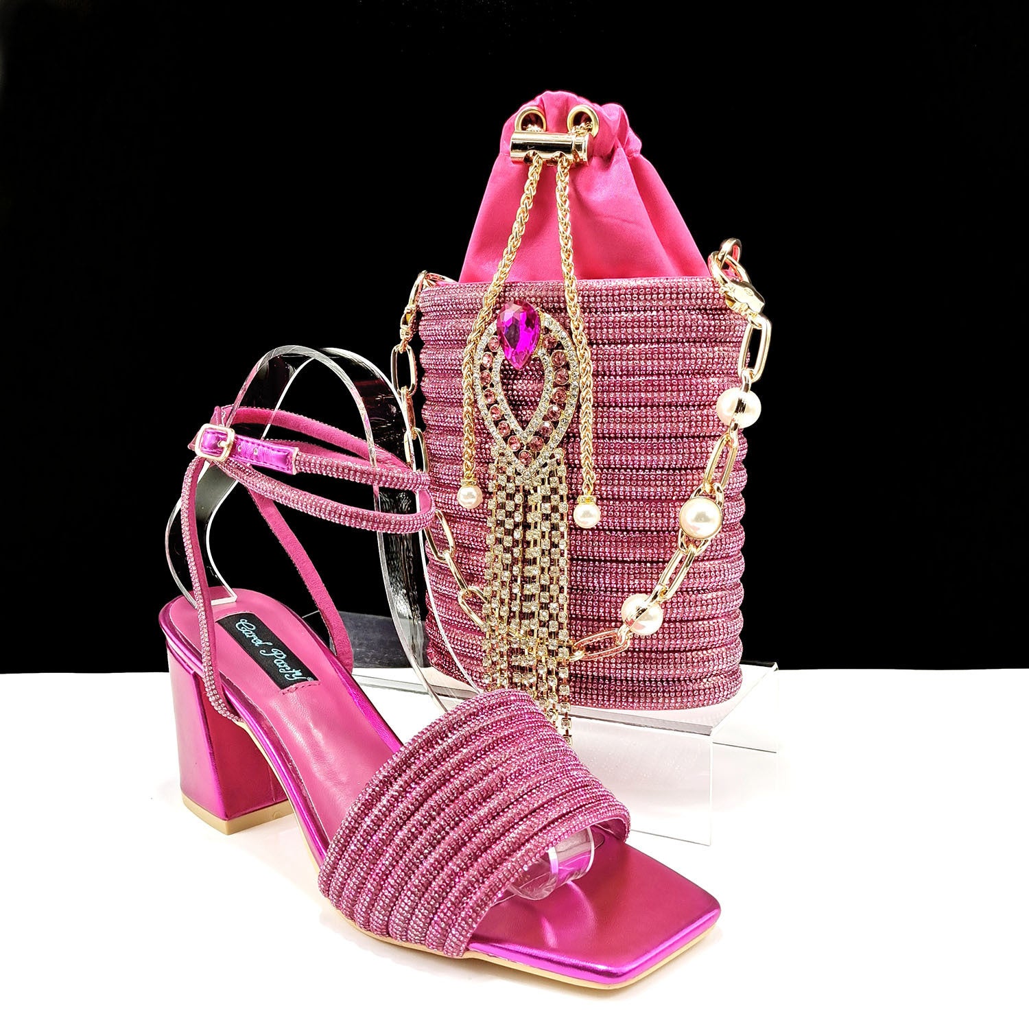 Pink high-heeled shoes and matching handbag with decorative chains on a black background
