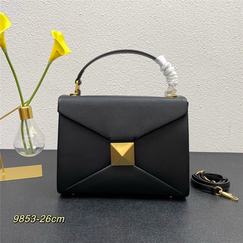 Black handbag with gold accents on a dark surface, featuring a white textured wall in the background.