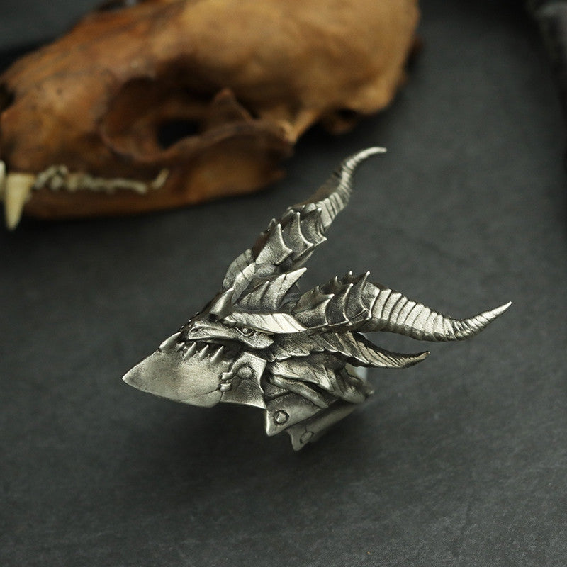 Silver dragon scale-like ornament on a dark surface with a blurred skull in the background