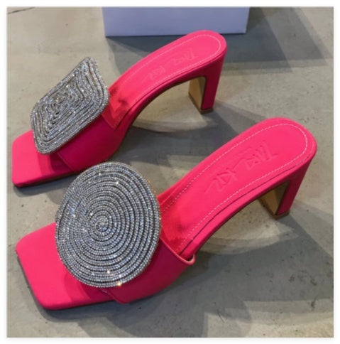 Pink high-heeled shoes with embellished straps on a concrete surface