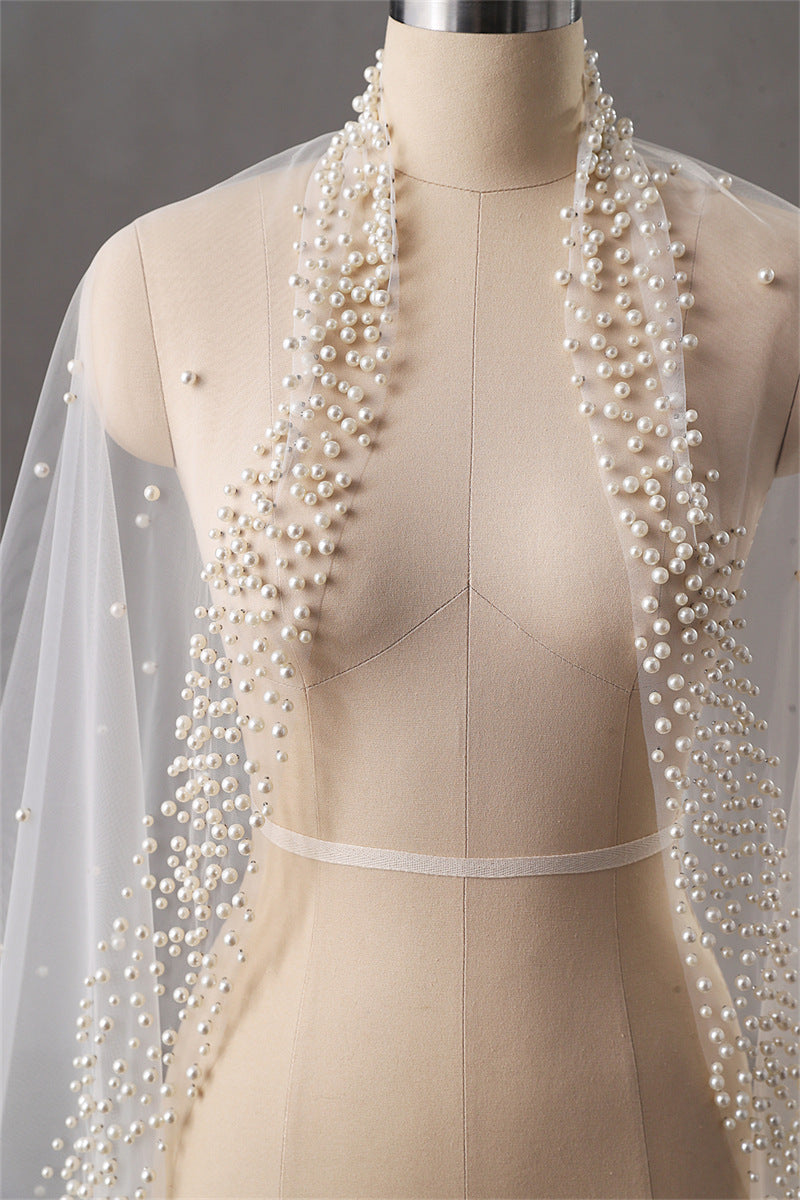 Mannequin wearing a beige dress with a long pearl necklace and veil.