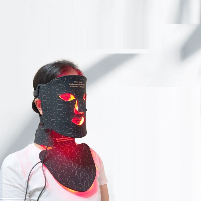 Person wearing a black face and neck massager with red lights on a white background
