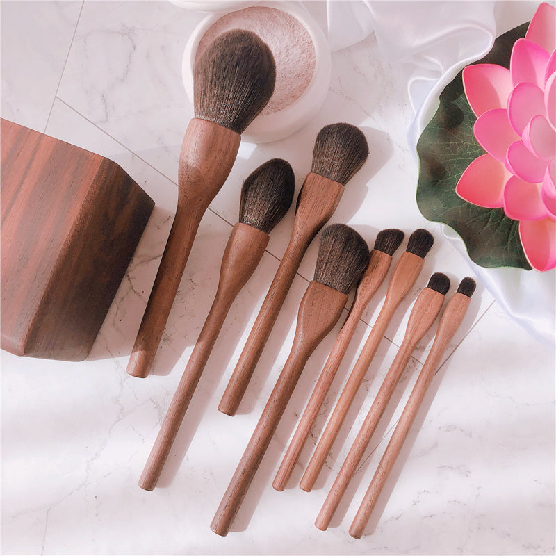 Set of wooden makeup brushes on a marble surface with a pink flower.