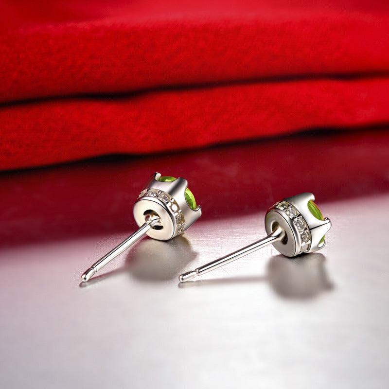 Silver earrings with green gemstones on a red fabric background