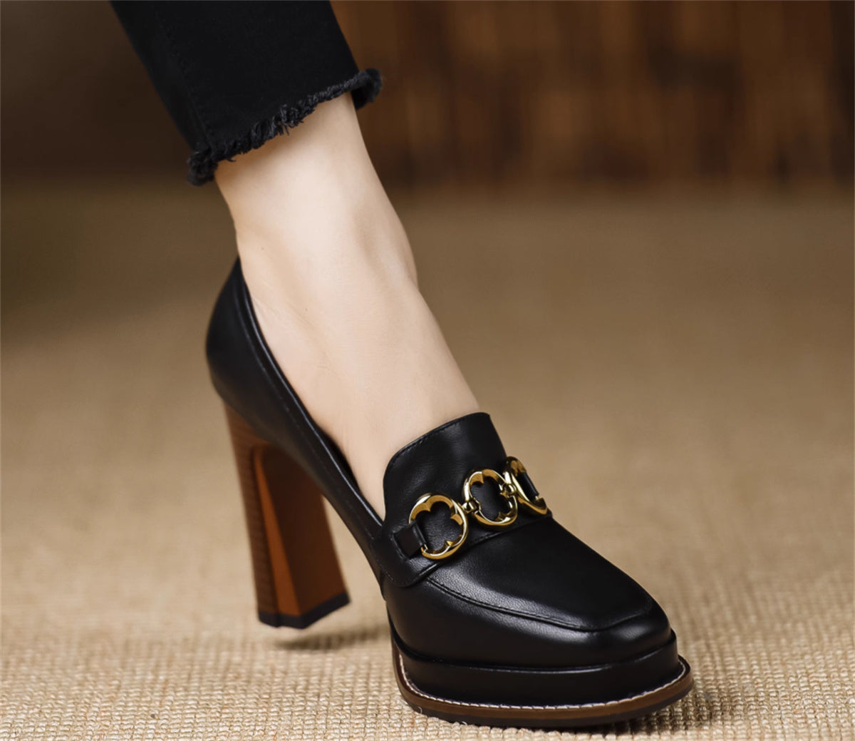 Black high-heeled shoes with gold buckles on a textured surface